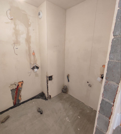 Jak wykończyć mieszkanie od dewelopera - zdjęcie przedstawia łazienkę w stanie deweloperskim z widocznymi odpływami kanalizacyjnymi 